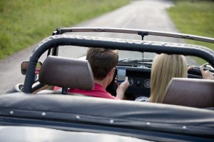 A young couple driving in the countryside, man looking navigating using a smartphone